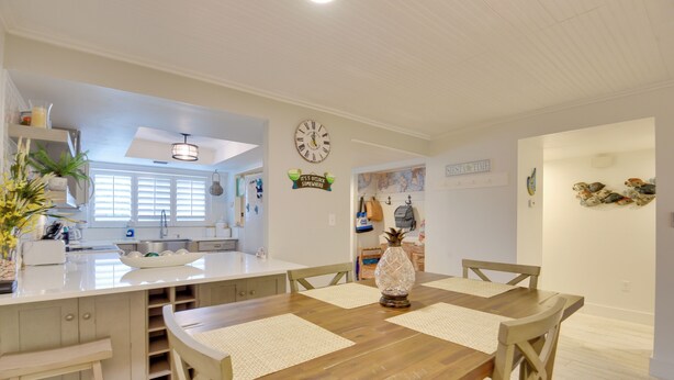A dining area with a wooden table, four chairs, and a decorative vase. There is a kitchen area with white cabinets and a clock on the wall. - Siesta Key Condo w/ Heated Pool < 1 Mi to Beach (Siesta Key)