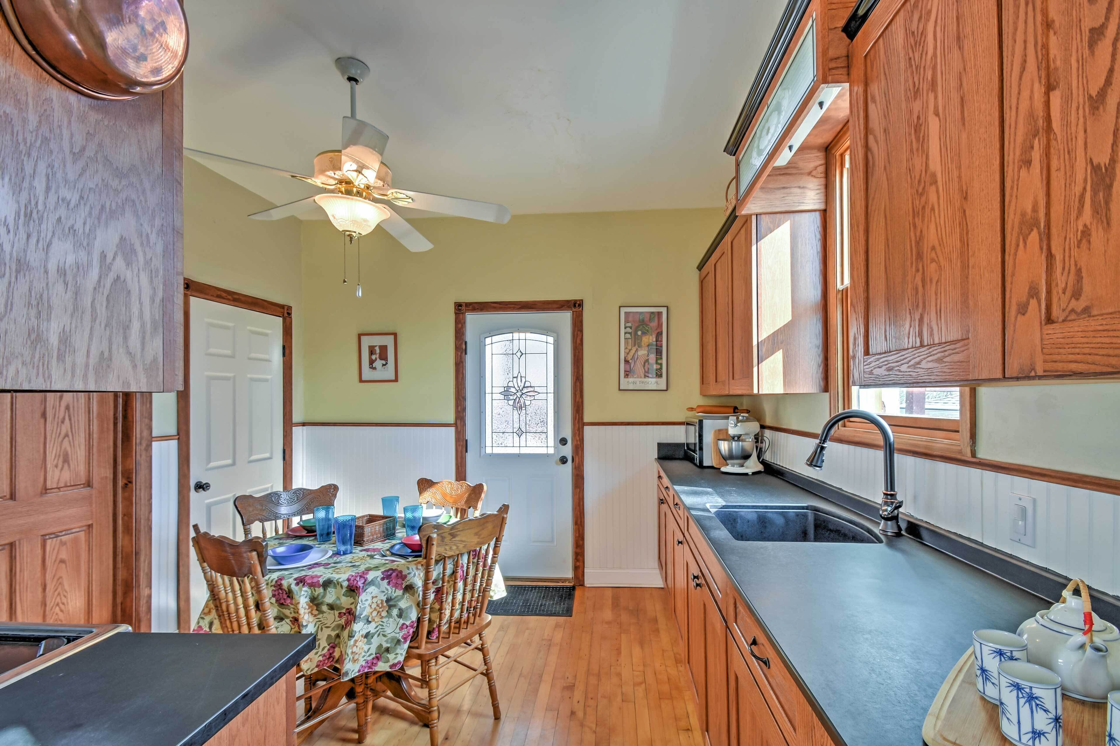 A kitchen with wooden cabinets, a dining table with chairs, a ceiling fan, and a window with a view.