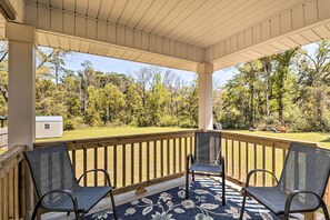A covered porch with two chairs and a small table, overlooking a grassy area with trees and a shed. - Magnolia Springs Cottage ~ 16 Mi to Beaches! (Magnolia Springs)