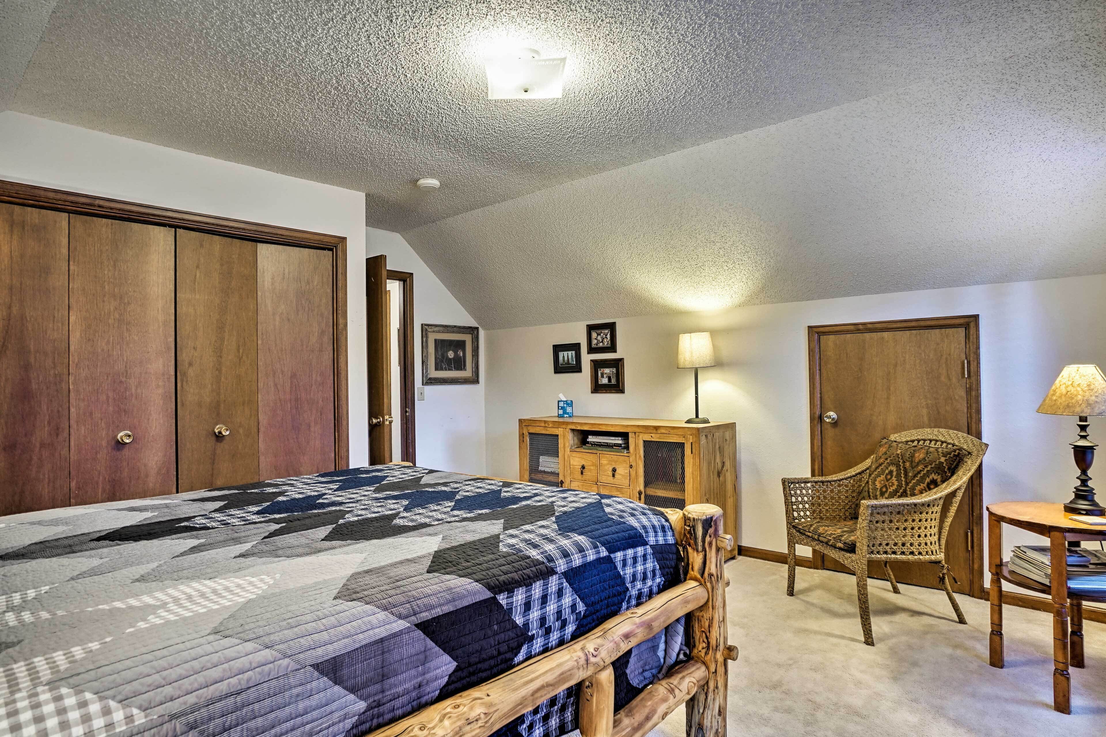 A bedroom with a large bed, wooden wardrobe, a wicker chair, a small table with a lamp, and a ceiling light.