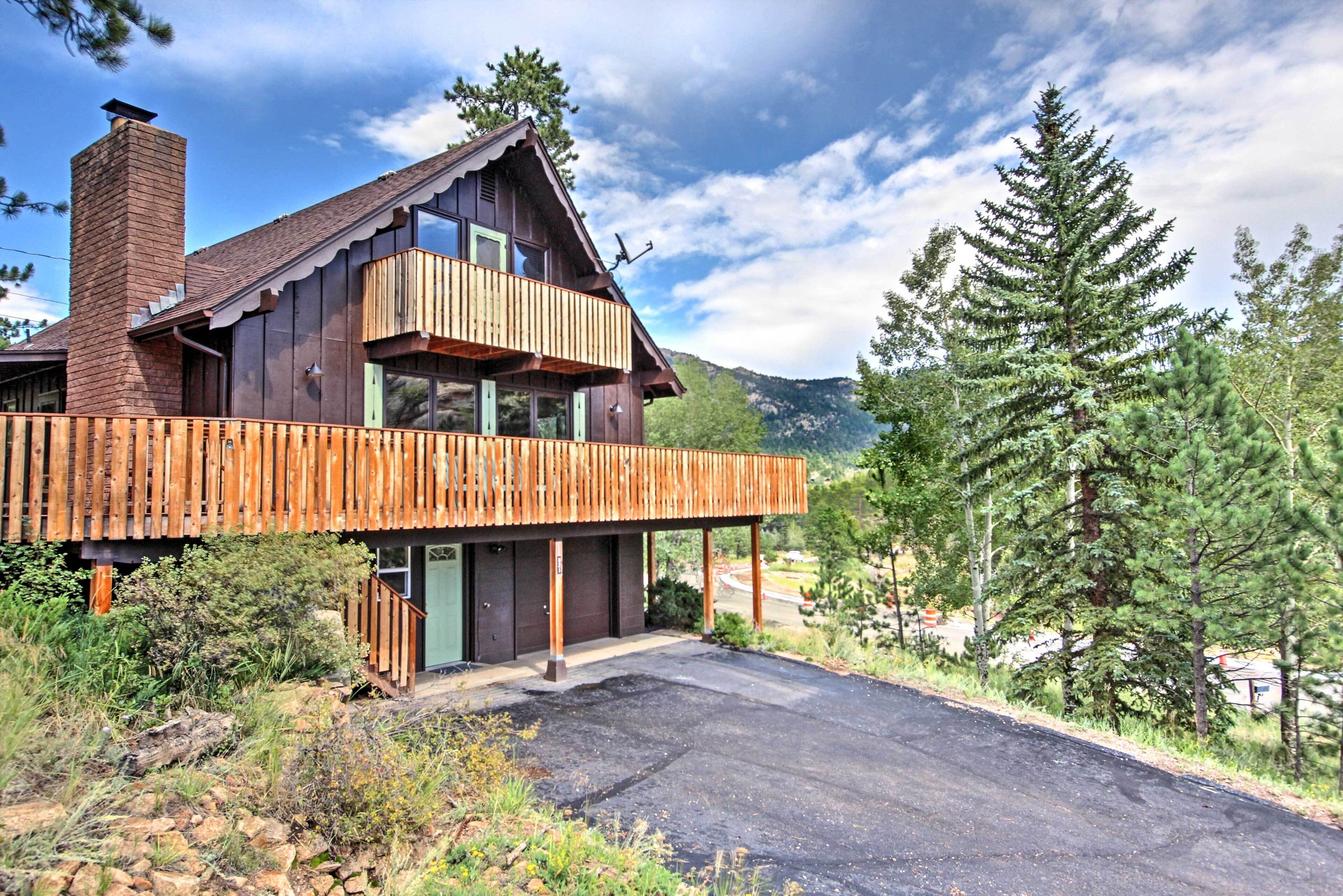 A wooden cabin with a balcony, a chimney, and a view of the surrounding forest and mountains.