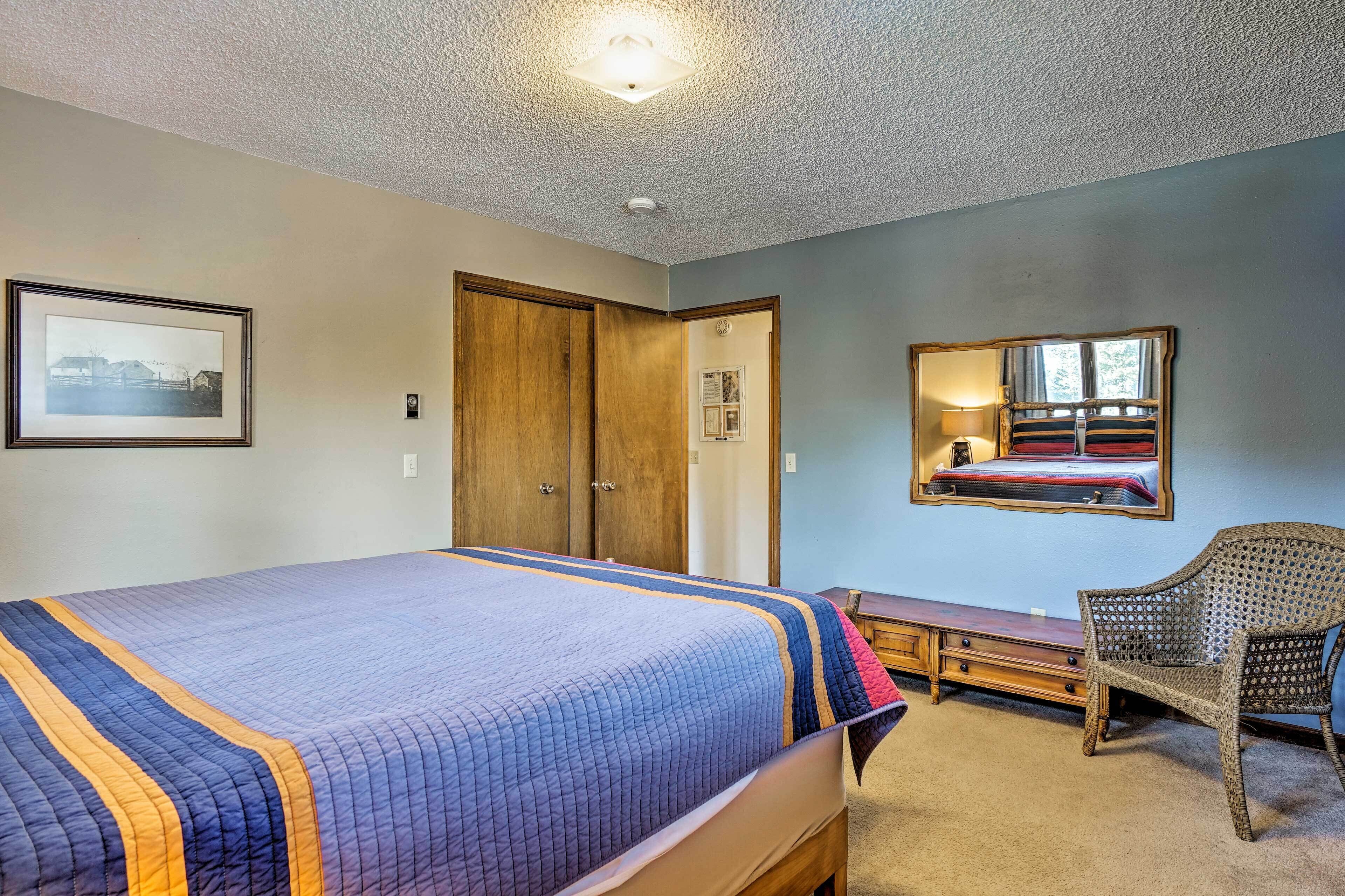 A bedroom with a large bed, a wooden wardrobe, a desk, and a wicker chair.