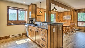 A kitchen with wooden cabinets, a central island, and a dining area with a table and chairs. - 'peaceful Pines' Estes Park Home: Longs Peak View (Estes Park)