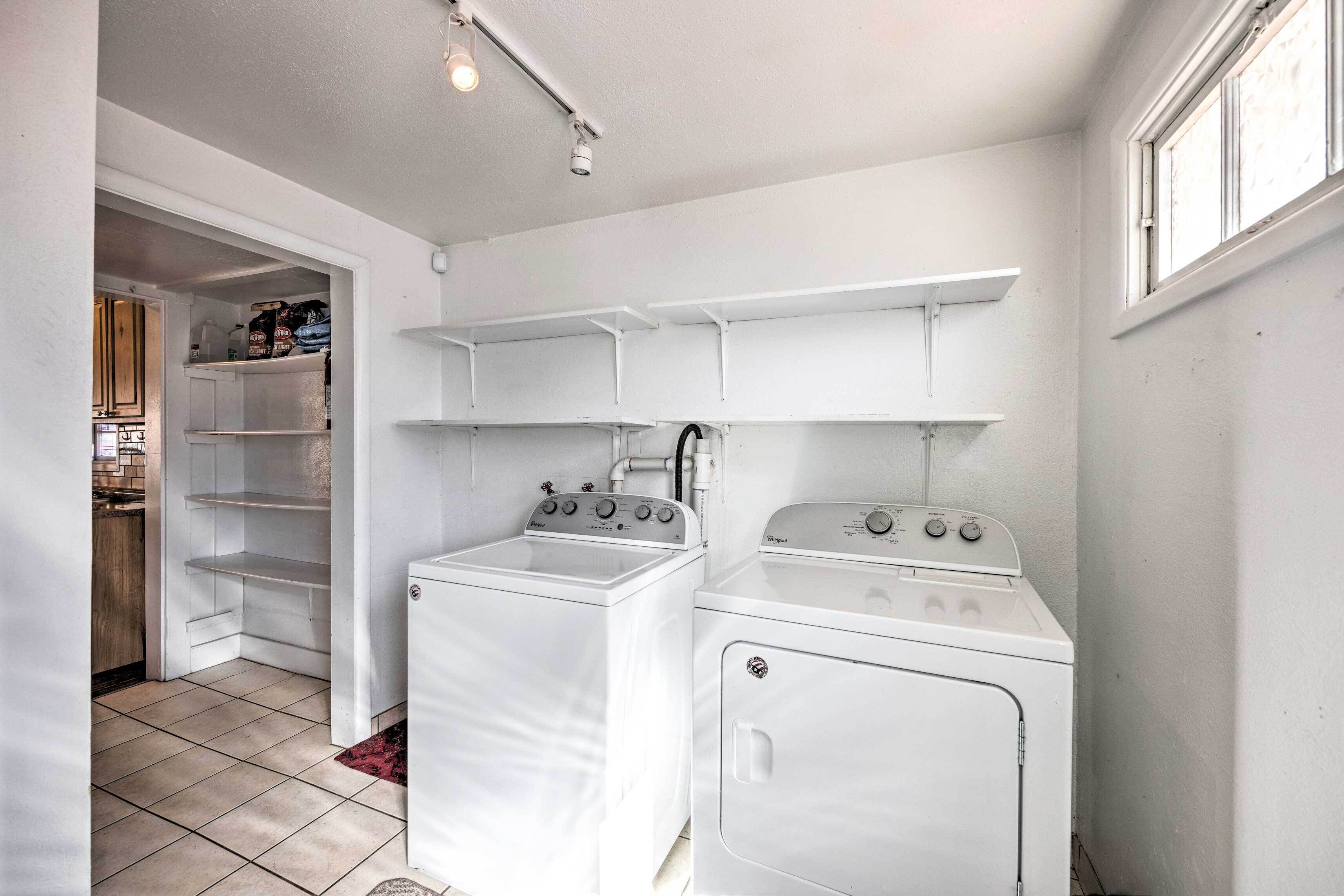 Une cuisine compacte équipée d’un lave-linge et d’un sèche-linge, d’un petit garde-manger et d’une fenêtre avec des stores.
