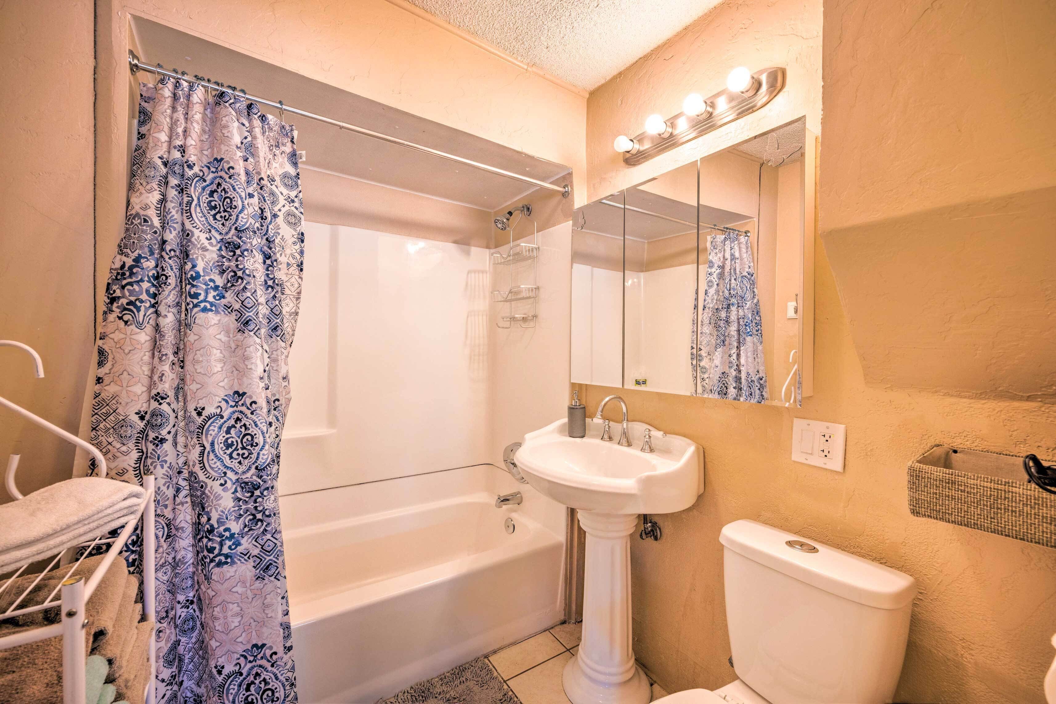 Une salle de bain avec une baignoire, un lavabo sur colonne, des toilettes et un miroir avec éclairage.