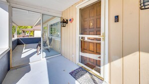 A covered porch with a sliding glass door, a wooden door with a brass handle, and a small outdoor light fixture. - Cozy Colorado Springs Home Near Garden of the Gods (Colorado Springs)