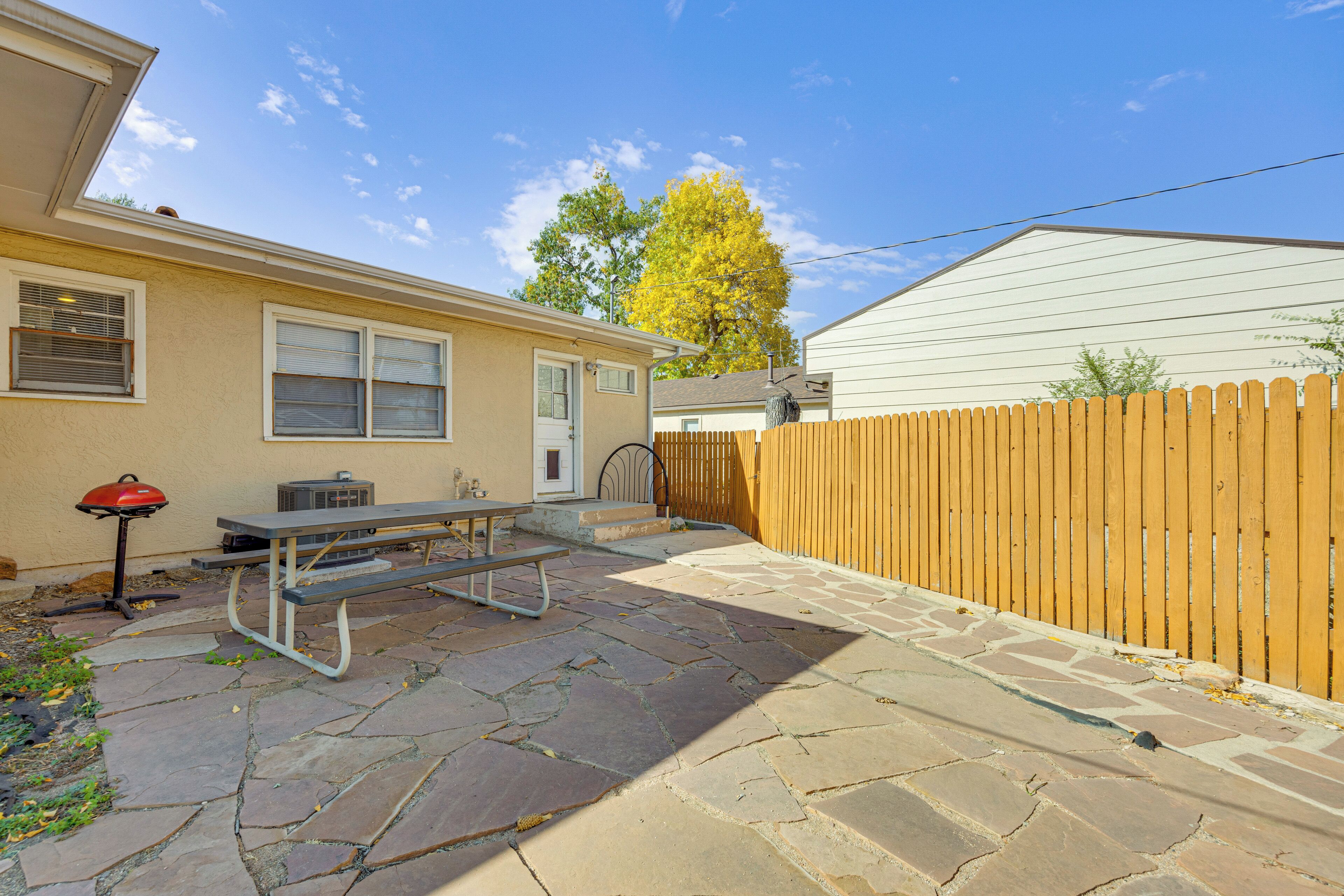 A patio with a picnic table and grill, a stone pathway, and a wooden fence.