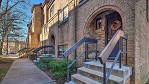 A brick building with a front entrance, a set of concrete steps with metal railings, and a clear sidewalk leading to the entrance.