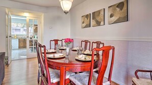 A dining area with a round wooden table, six chairs, and a chandelier. There are three wall-mounted artworks above the table.