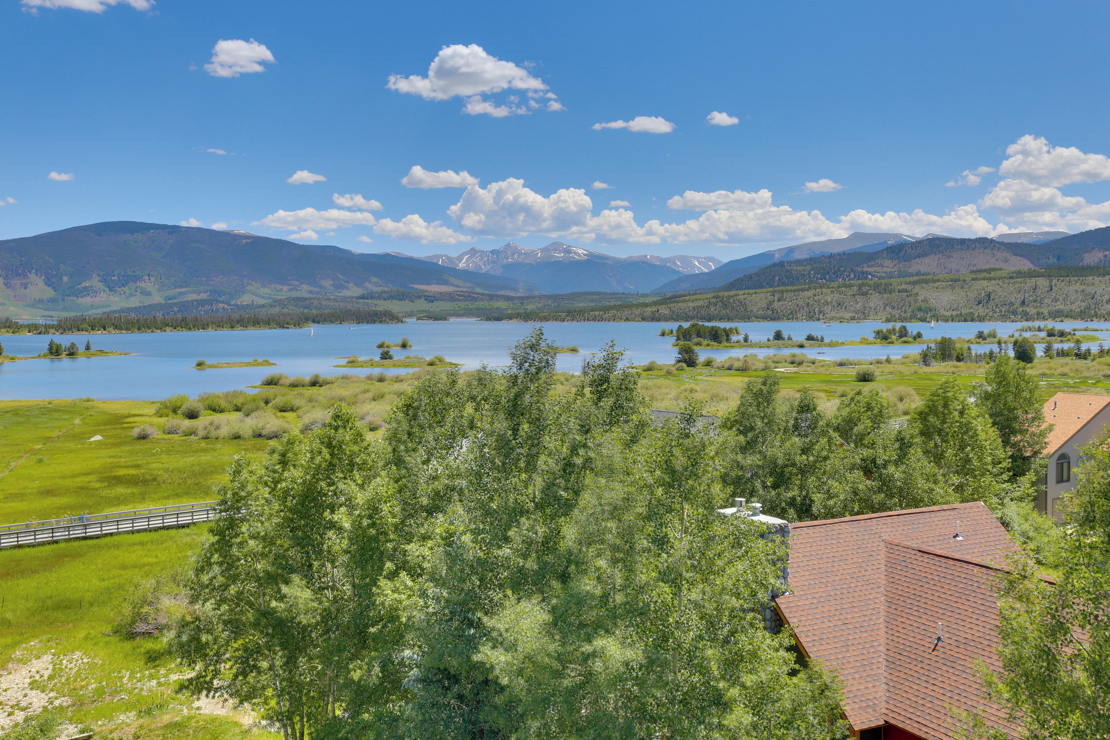 Une propriété au bord du lac, offrant une vue sur les montagnes, avec une terrasse en bois et un bâtiment doté d’un toit rouge.