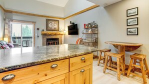 A kitchen with wooden cabinets, a granite countertop, a fireplace, and a dining area with stools. - Ski & Relax Fireside: Frisco Gem w/ Resort Perks! (Frisco)