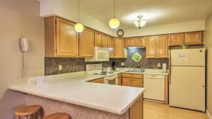 A kitchen with wooden cabinets, a white countertop, a microwave, a stove, a refrigerator, and two bar stools. - Lincoln Resort Condo w/ Pool Access - Near Hiking! (Lincoln)