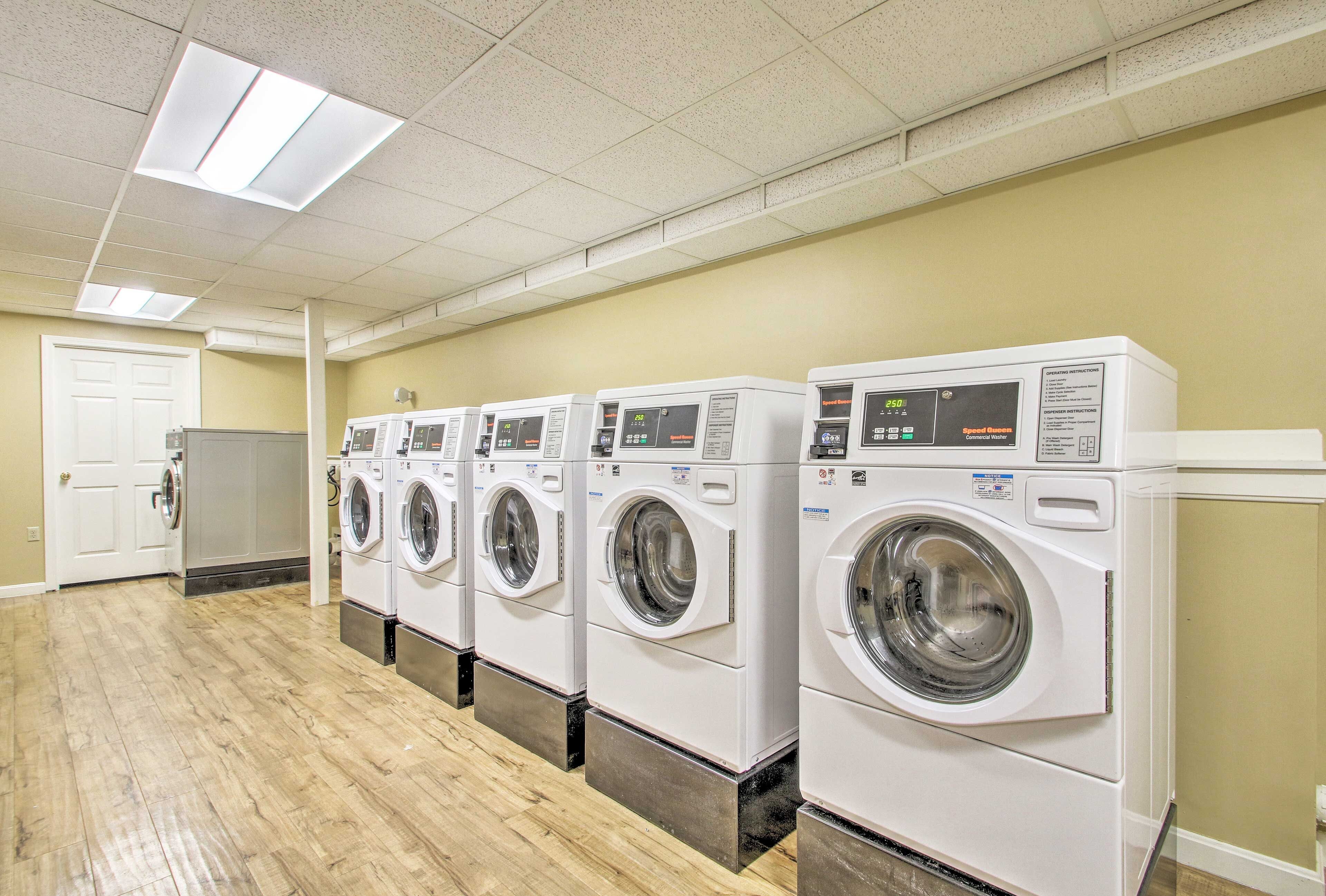 A row of front-loading washing machines in a laundry room with a wooden floor and a door in the background.