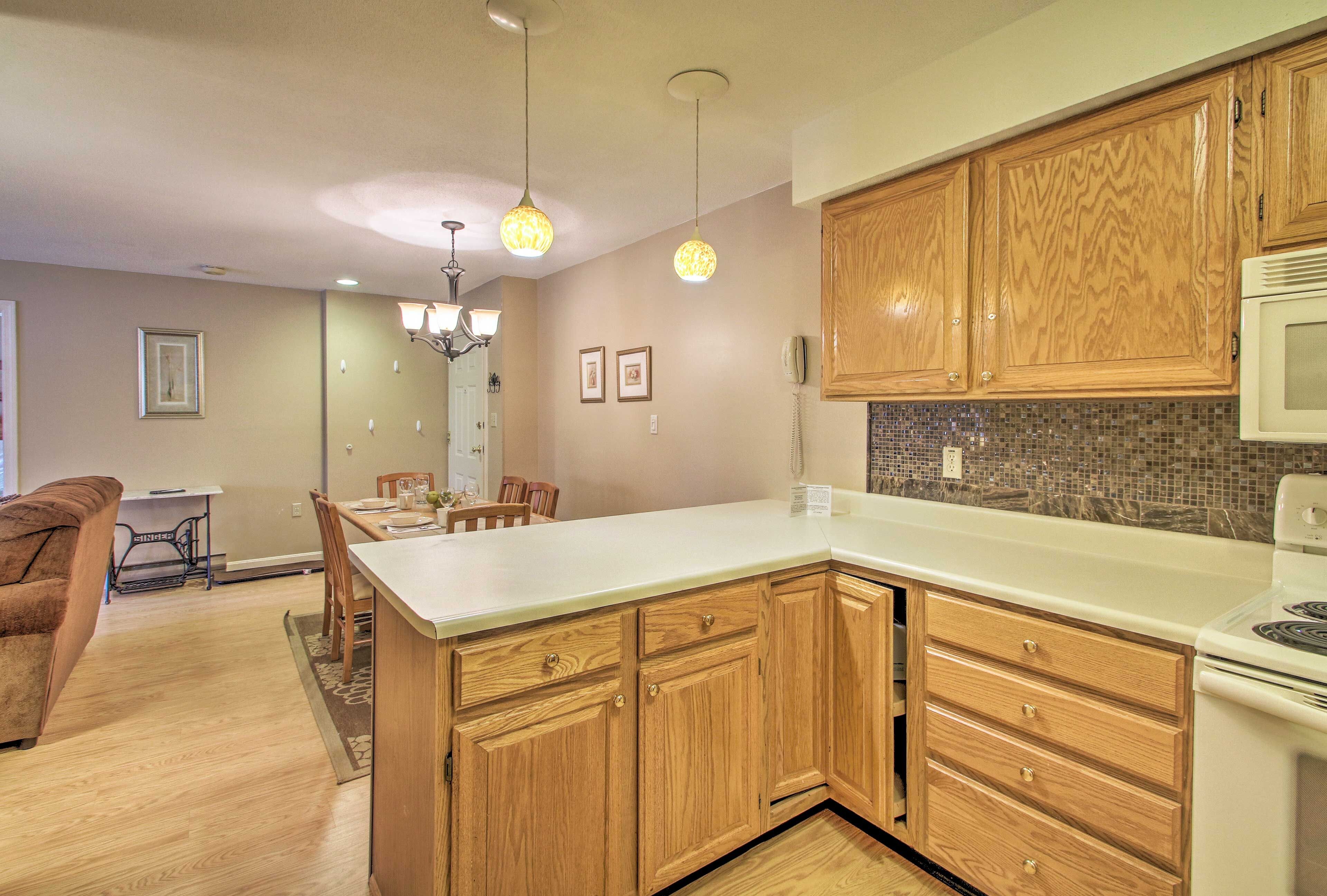 A kitchen with wooden cabinets, a white countertop, and a microwave. There is a dining area with a table and chairs.
