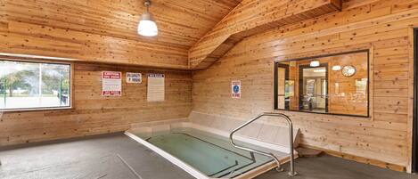 Un spa de madera con una bañera de hidromasaje cubierta de cristal, paredes de madera y un reloj en la pared.