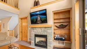 Een woonkamer met een stenen openhaard, een wandtelevisie en houten planken.