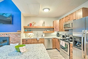 Una cocina moderna con encimeras de granito, electrodomésticos de acero inoxidable, armarios de madera y una pared de ladrillo decorativa.