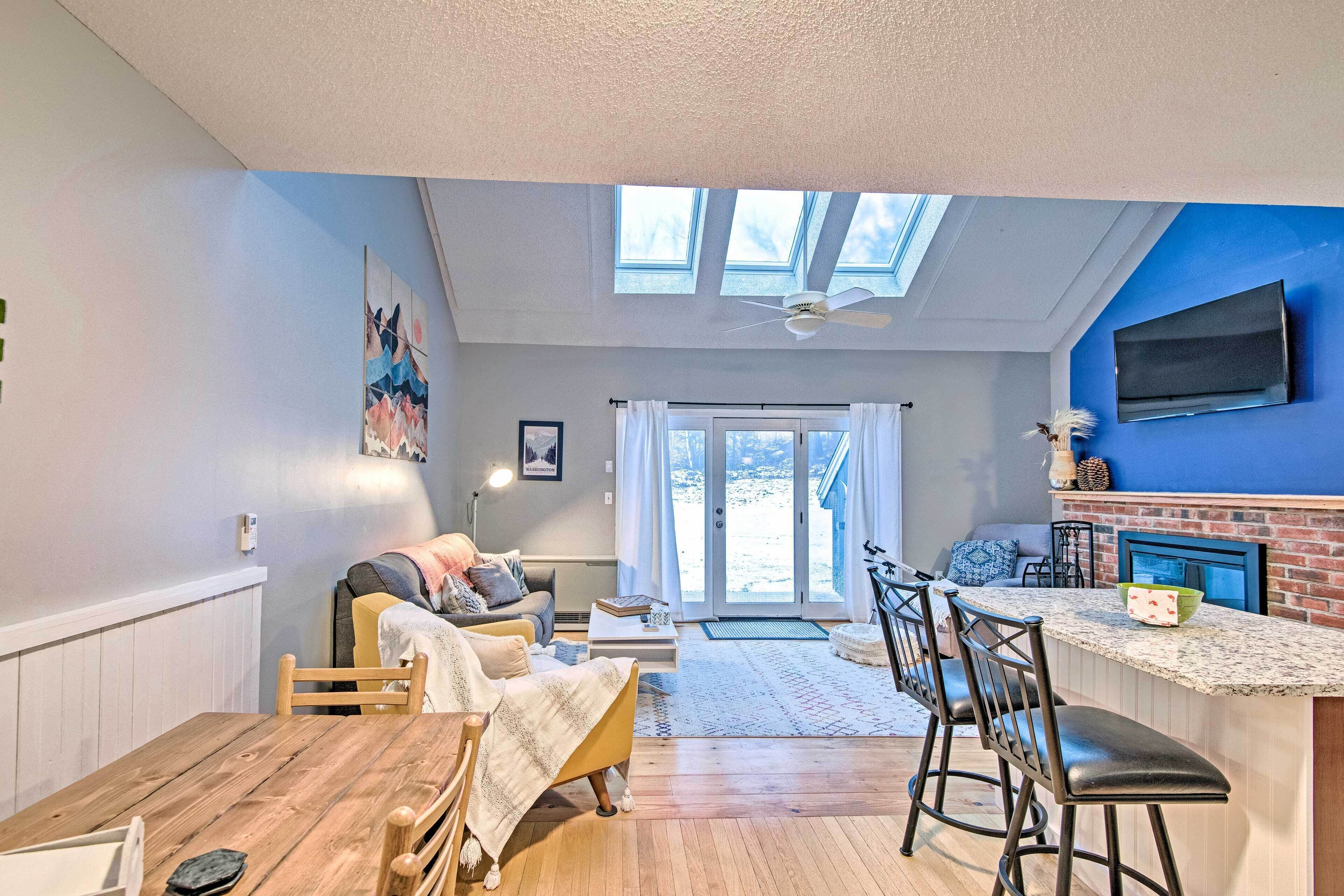 A cozy living room with a wooden dining table, a sofa, and a kitchen area with a TV and fireplace.