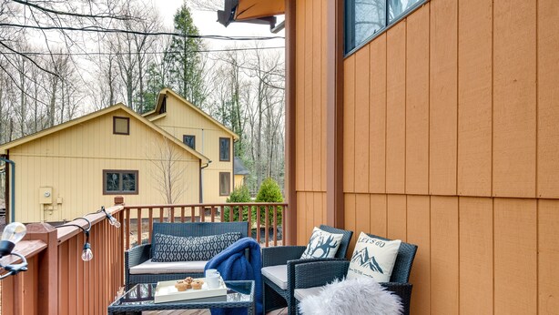 Une terrasse en bois avec des meubles d’extérieur, une table en verre et, en arrière-plan, une maison jaune.