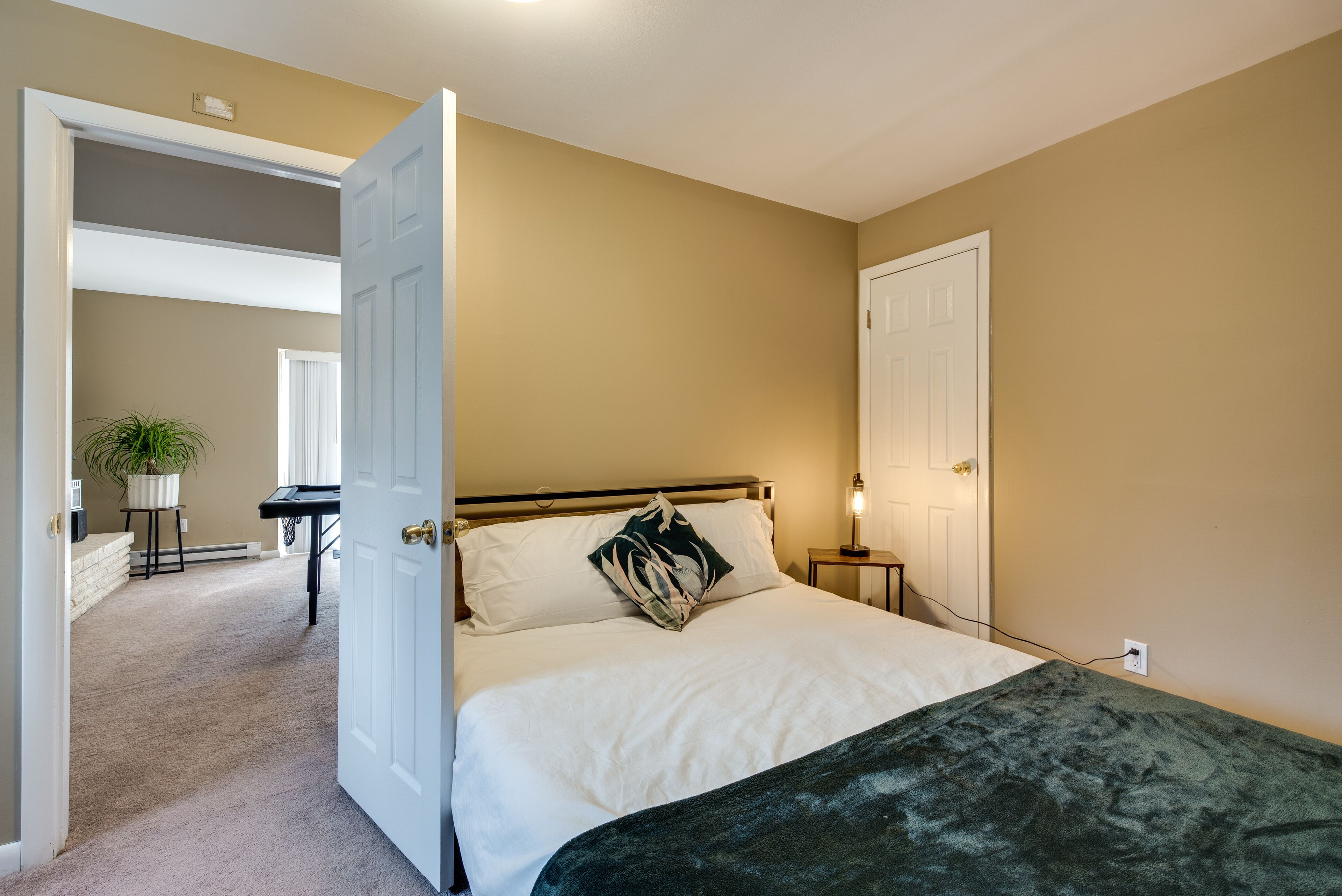 A bedroom with a bed, a nightstand, a lamp, and a door leading to another room.