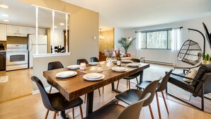 Un espace repas moderne avec une table en bois, des chaises noires et une cuisine en arrière-plan.