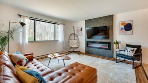 Un salon moderne avec un canapé en cuir, un fauteuil suspendu, une cheminée et une grande fenêtre.