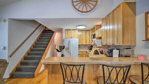 A kitchen with wooden cabinets, a refrigerator, a coffee machine, and a bar area with chairs.