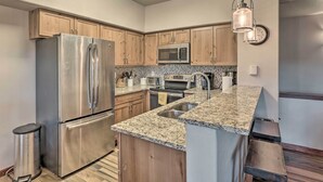 A modern kitchen with stainless steel appliances, wooden cabinets, granite countertops, and a hanging light fixture. - The Chelsea Condo w/ Hot Tub & Pool Access! (Breckenridge)