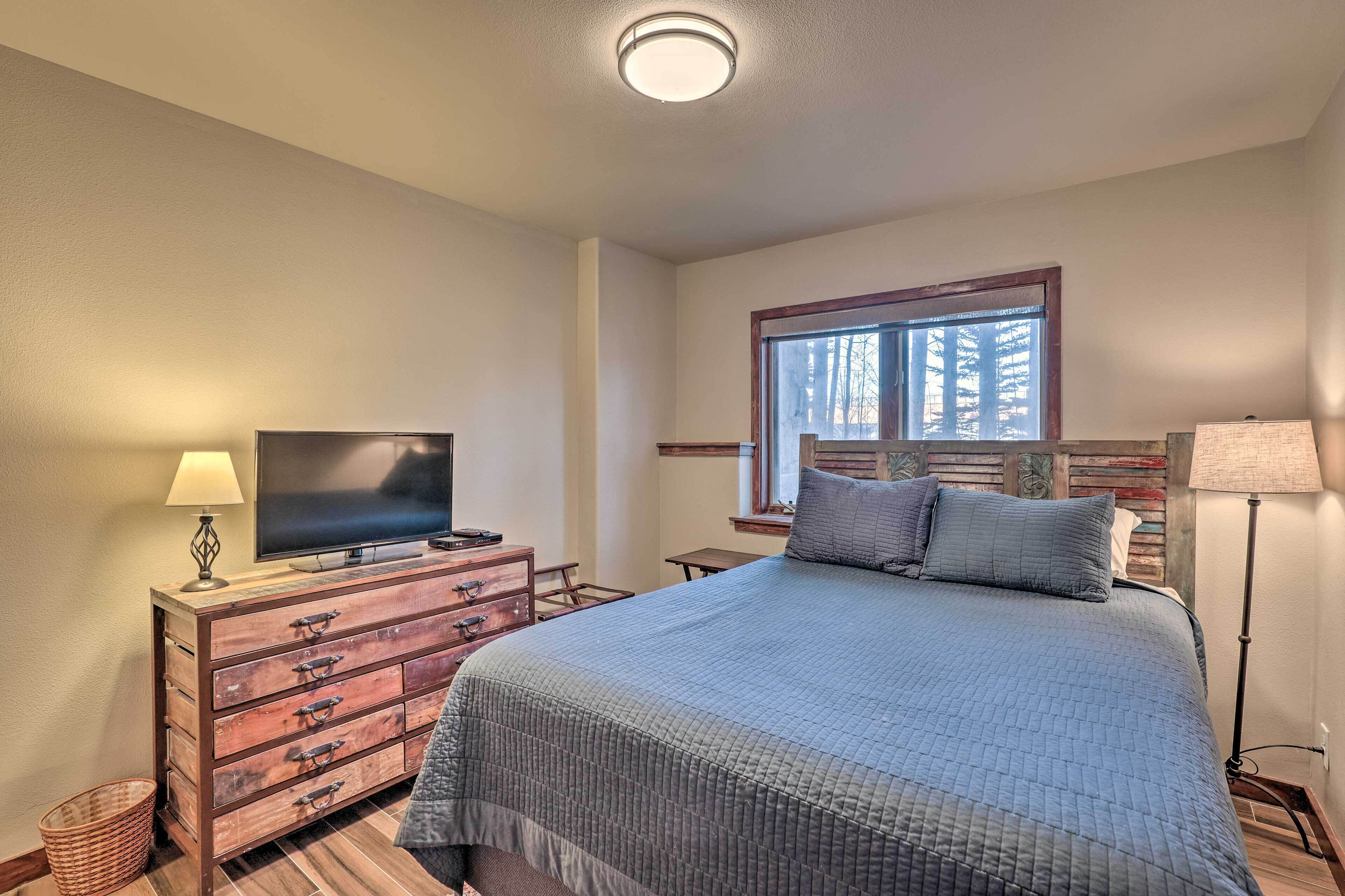 Une chambre à coucher avec un lit, une commode, une télévision, une fenêtre et une lampe.