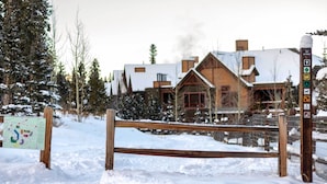 A wooden bench in a snowy area with a signpost and a building in the background. - The Chelsea Condo w/ Hot Tub & Pool Access! (Breckenridge)