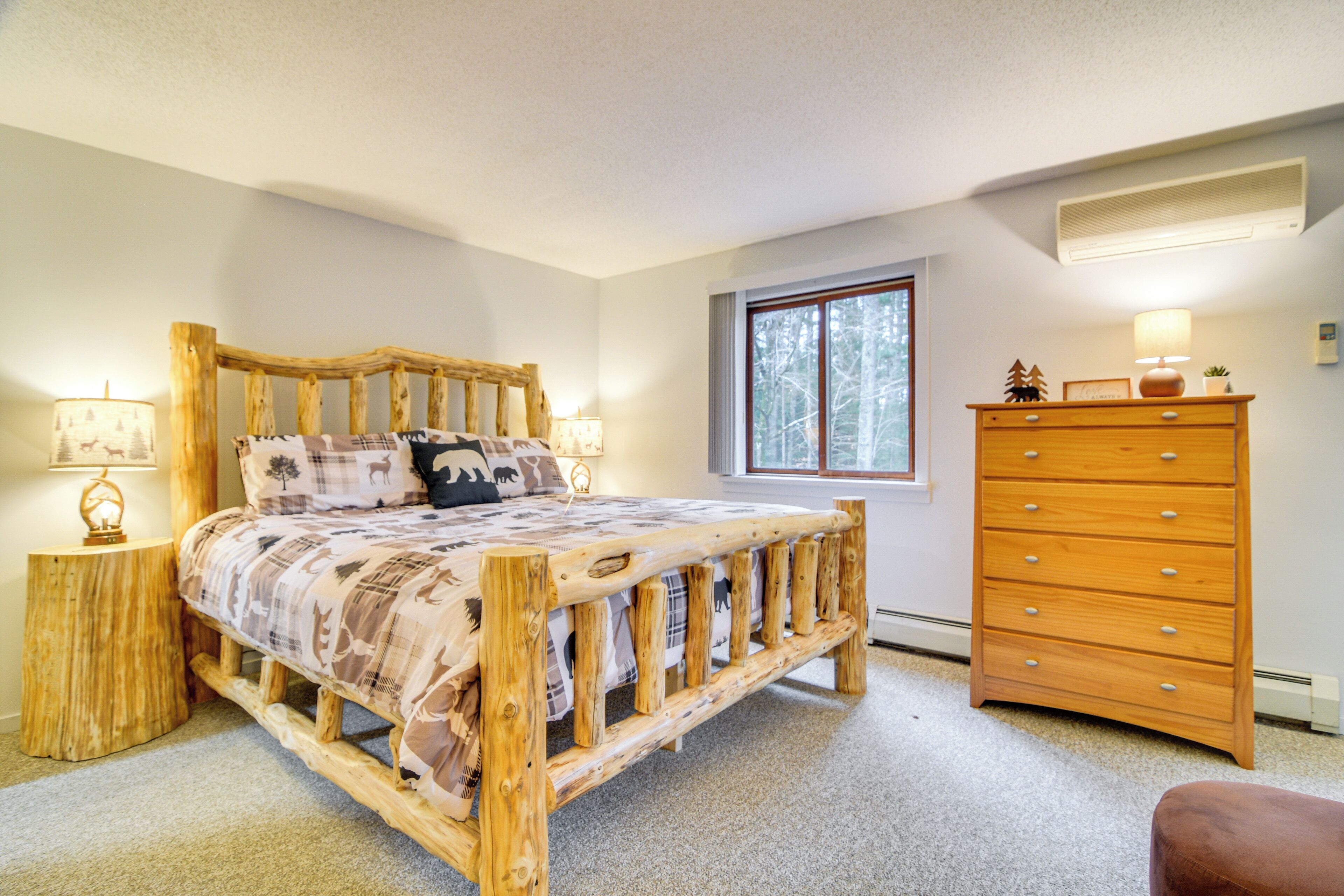 A bedroom with a wooden bed frame, a dresser, and a window with a view of trees.