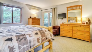 A bedroom with a large bed, a wooden dresser, a mirror, and a television on the wall. - Cozy Bartlett Condo w/ Deck & Resort Amenities! (Bartlett)