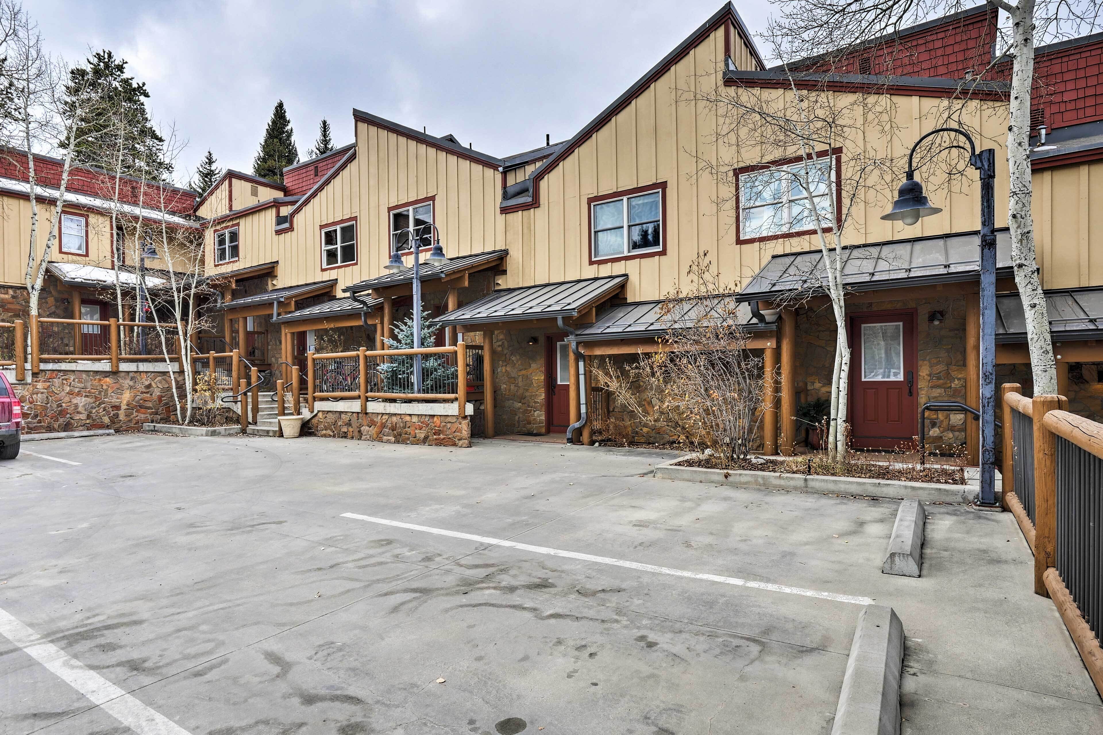 A row of wooden buildings with stone facades, a parking area, and a clear sky.