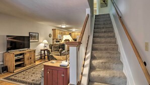 A living room with a TV, wooden entertainment unit, and a rug. A staircase with a wooden handrail leads to a kitchen area with wooden cabinets and a microwave. - Ski-in/out Condo! Walk to Main Street Breckenridge (Breckenridge)
