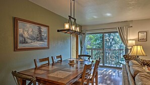 A dining area with a wooden table and chairs, a chandelier, a painting of a snowy mountain, and a view through a glass door to an outdoor deck. - < 2 Mi to Frisco Adventure Park: Cozy Townhome! (Frisco)