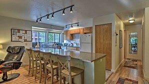 A modern kitchen with wooden cabinets, a central island with bar stools, and a dining area. - < 2 Mi to Frisco Adventure Park: Cozy Townhome! (Frisco)
