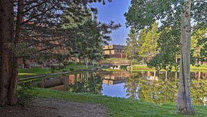 A serene lakeside view with a wooden bridge, a grassy area, and a building in the background. - < 2 Mi to Frisco Adventure Park: Cozy Townhome! (Frisco)