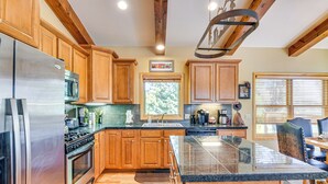 A modern kitchen with wooden cabinets, stainless steel appliances, a large island, and a dining area with a view of the outdoors. - 1 Mi to Grand Lake: Family-friendly Gem w/ Hot Tub (Grand Lake)