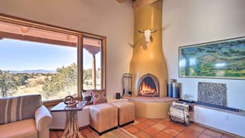 A cozy living room with a fireplace, a large window overlooking a scenic landscape, and a rustic ceiling.