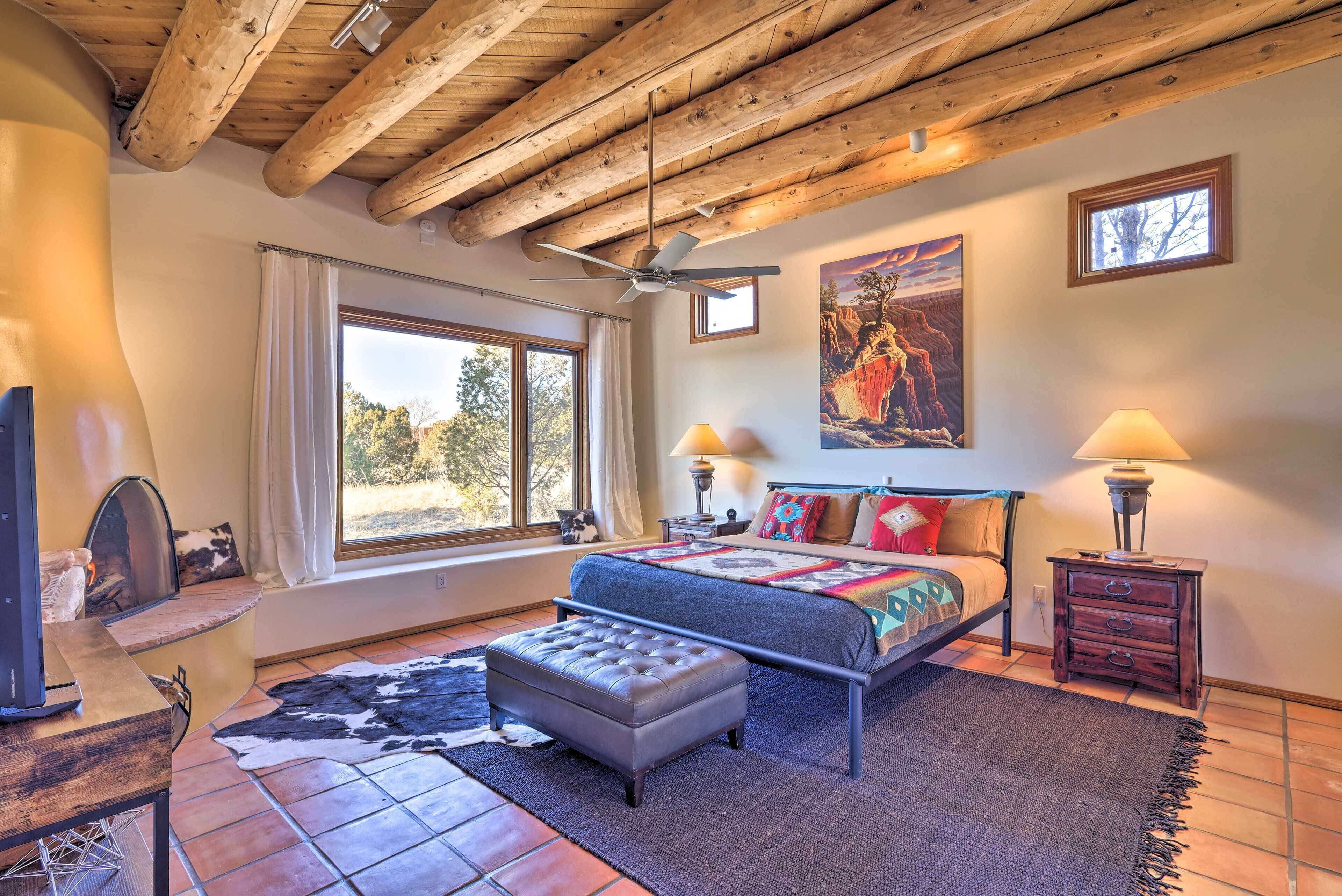 A bedroom with a bed, a ceiling fan, a window, a lamp, and a painting on the wall.