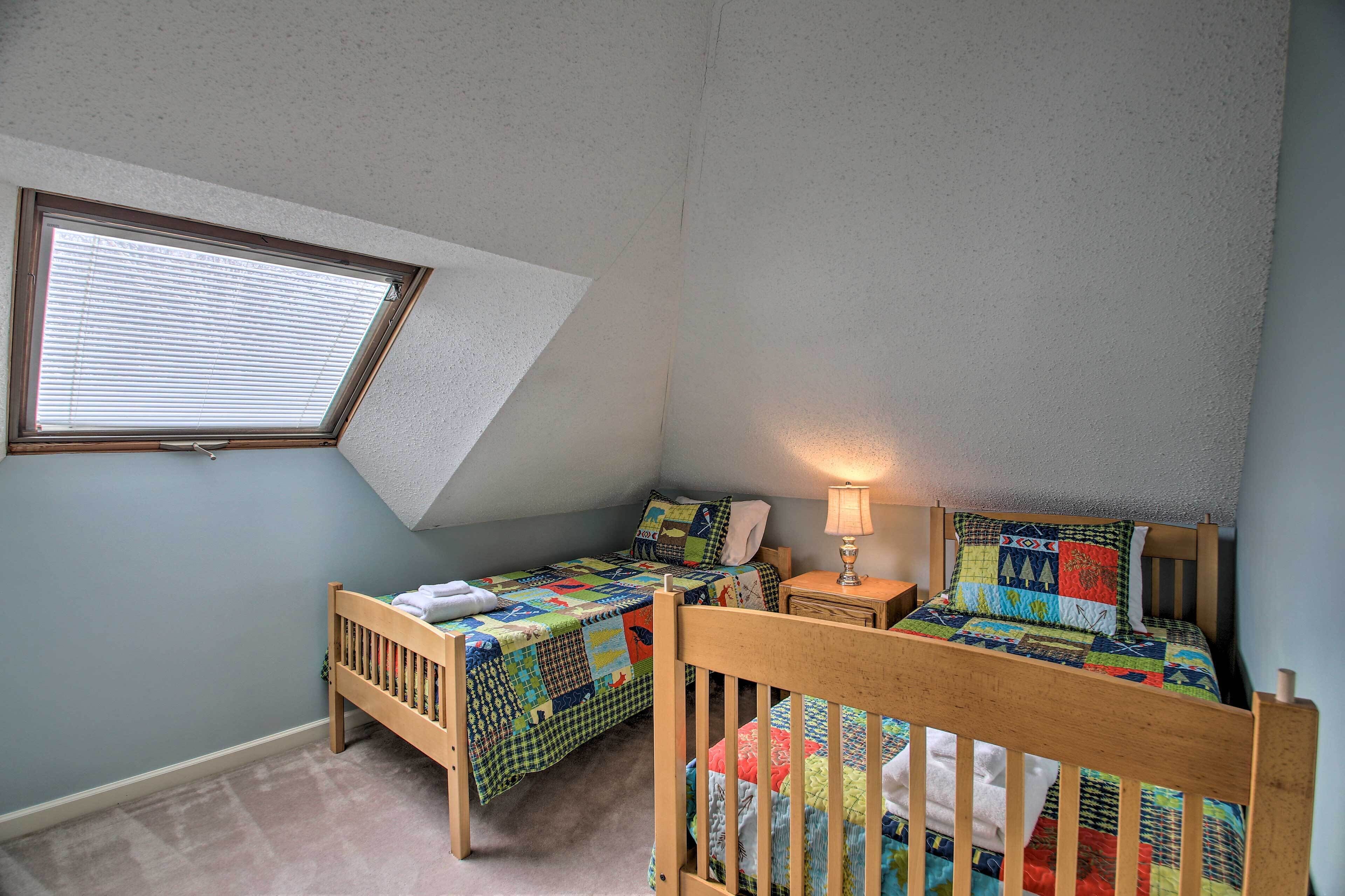 A small, cozy bedroom with two single beds, a nightstand, a lamp, and a window with blinds.