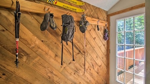 Et træpanelt interiør med ski og skibeklædning hængende på væggen, et vindue med udsigt til en terrasse, og en dør.