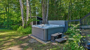 Un bain à remous situé dans un espace boisé, avec une terrasse en bois et un petit abri de jardin.
