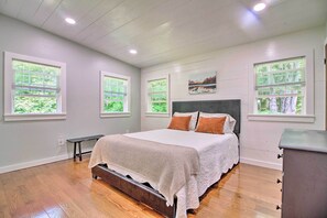 A bedroom with a large bed, a bench, and a dresser. There are three windows with blinds, and a painting on the wall. - Stylish Mountain Home Near Ski, Golf + Manchester! (Bondville)