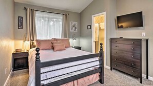 A bedroom with a bed, bedside tables, a dresser, a TV, and a window with curtains.