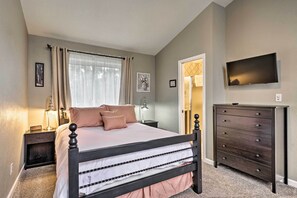 Une chambre à coucher avec un lit, des tables de chevet, une commode, un téléviseur et une fenêtre avec des rideaux.