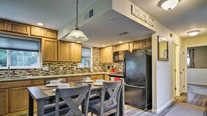 A modern kitchen with wooden cabinets, a granite countertop, and a built-in stove. There is a dining table with chairs and a hanging light fixture.