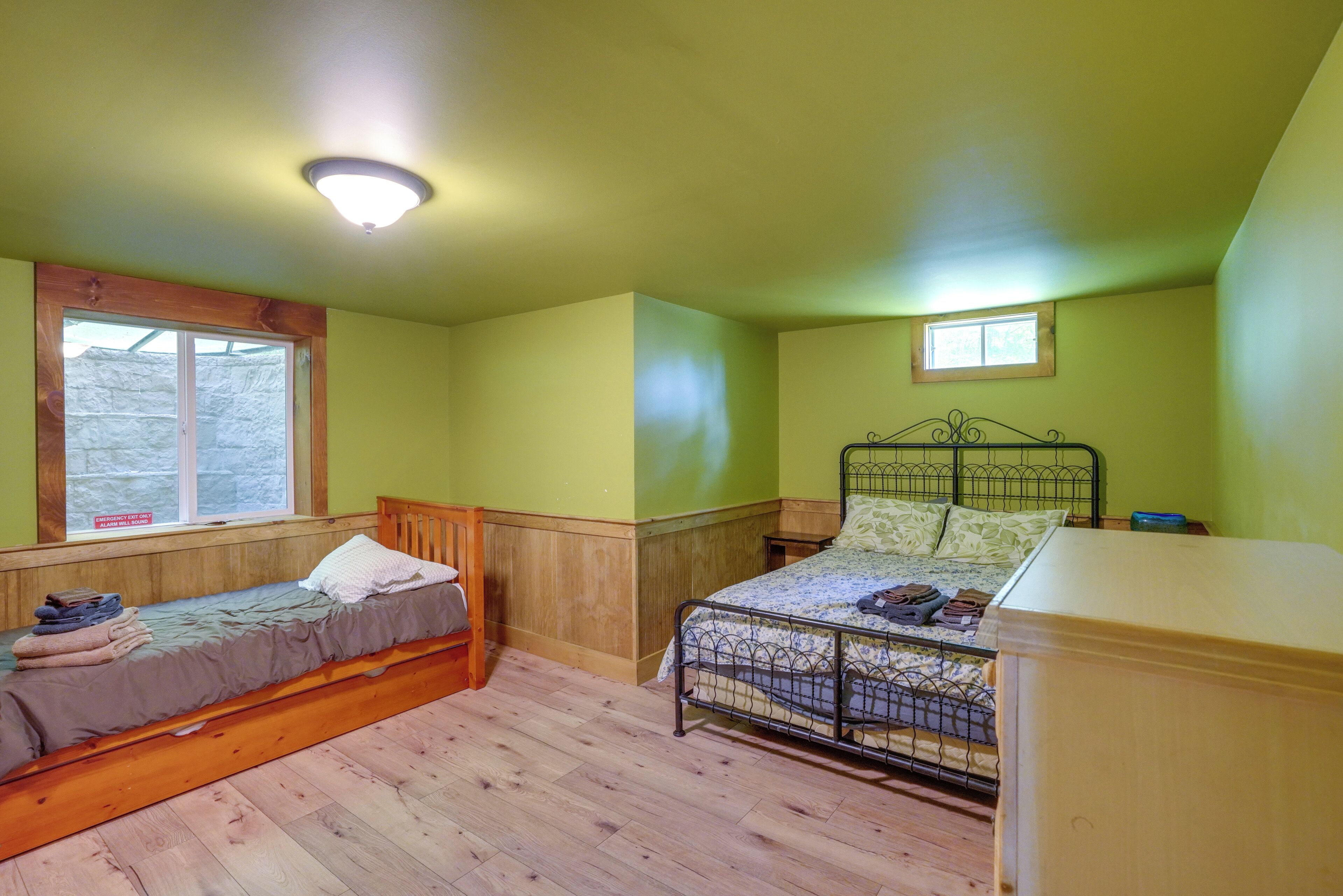 A room with two beds, wooden flooring, a window, and a ceiling light.