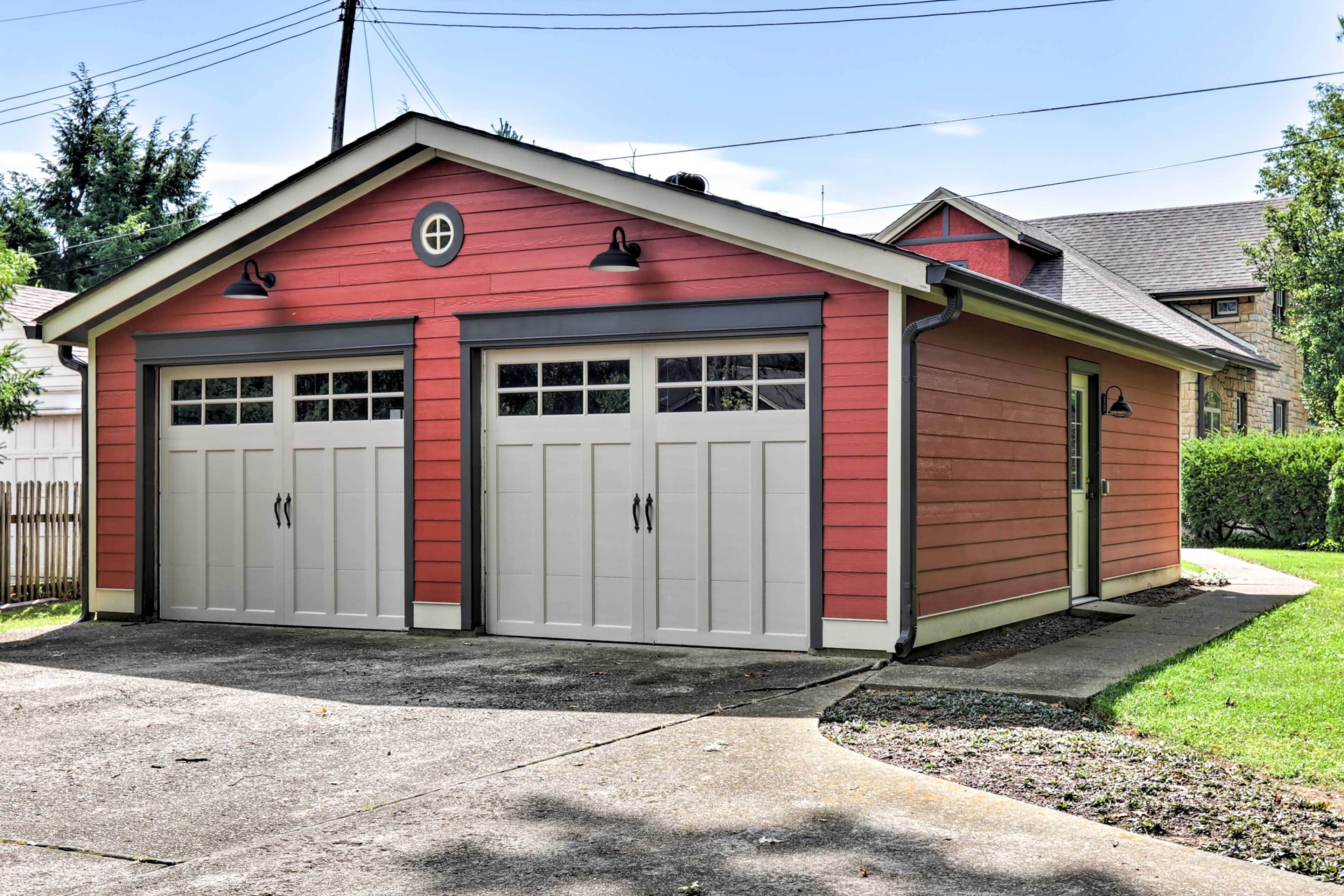Un garage pour deux voitures, avec une façade rouge et une porte blanche, attenant à une maison dotée d’un toit à pignon.