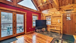 L’intérieur d’une cabane est doté d’un plafond en bois, de grandes fenêtres, d’un téléviseur et d’une cheminée en pierre.